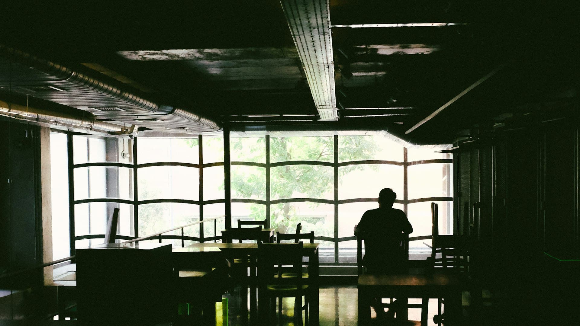 A quiet lounge in warm dim light, a single figure at the window