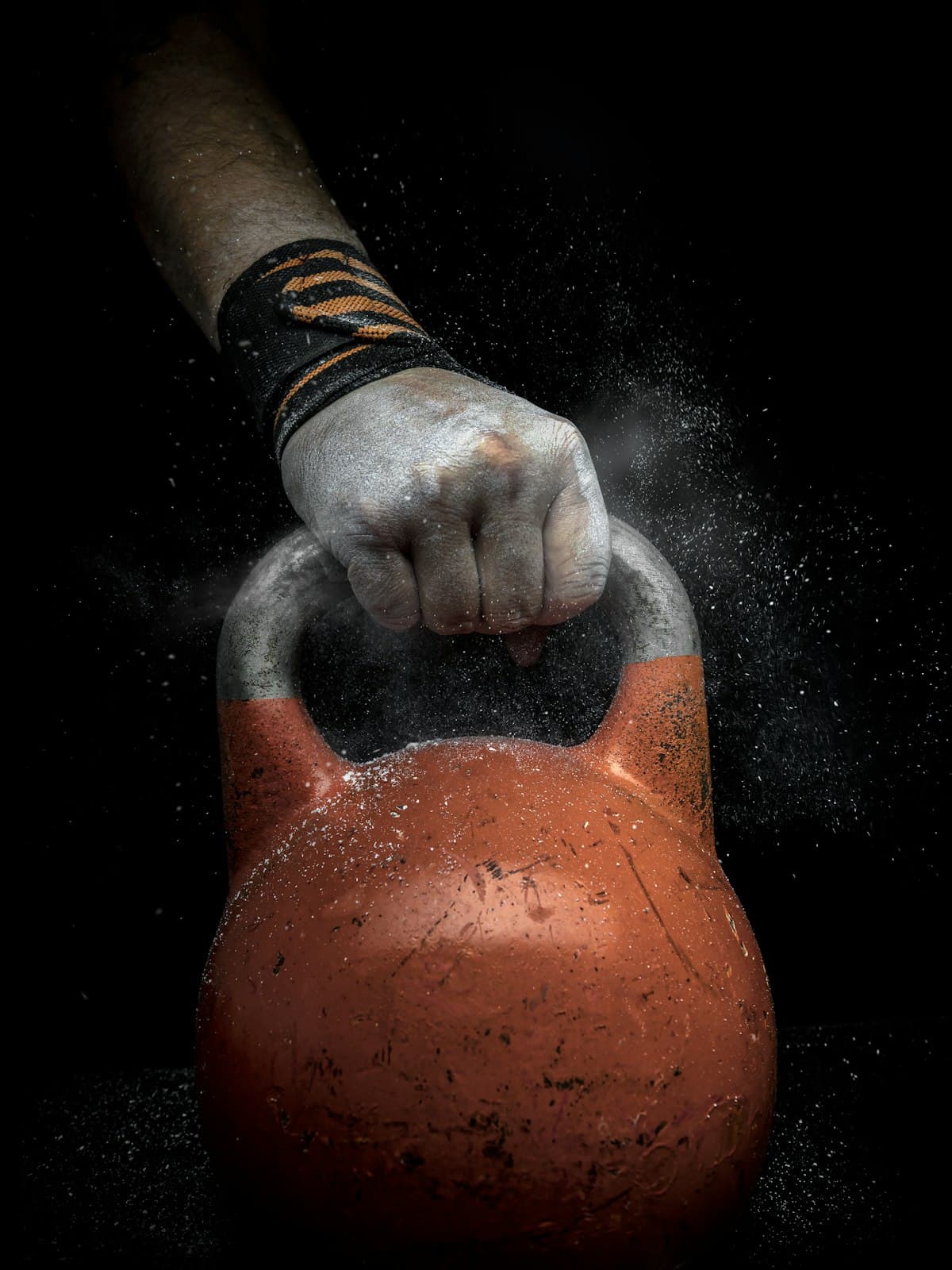 A chalked hand gripping a kettlebell against black