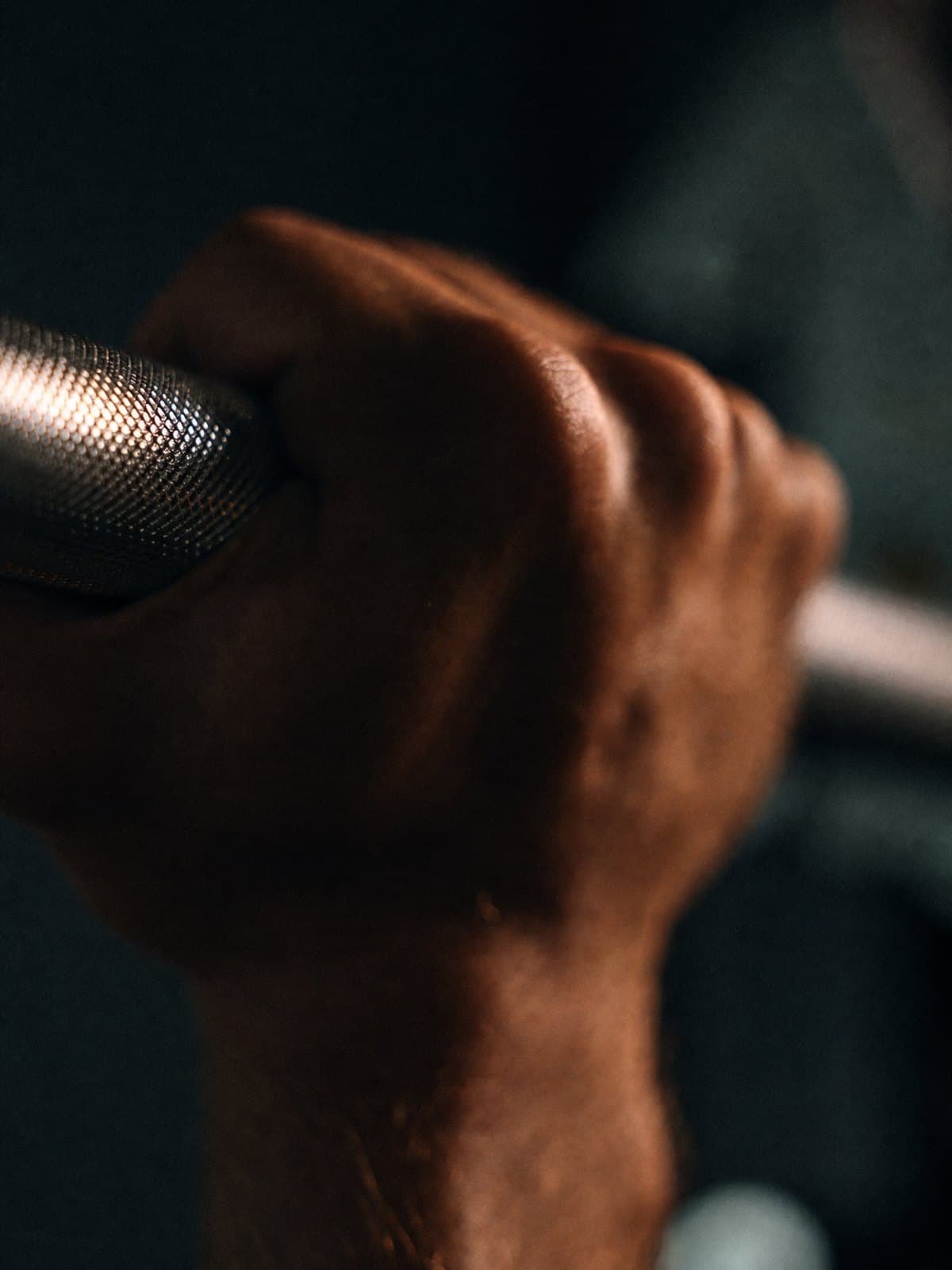 A hand closed around a dumbbell handle, lit against deep shadow