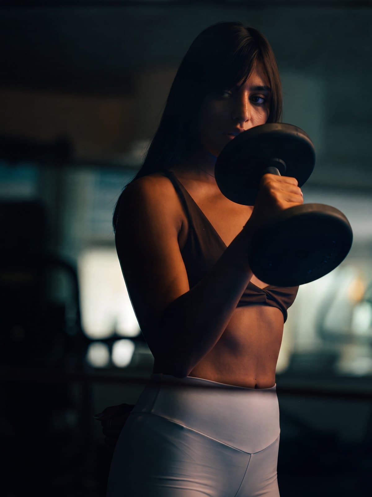 A member curling a dumbbell, lit warm against a dark floor
