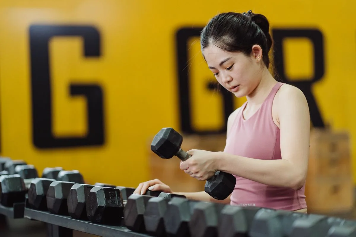 Woman lifting dumbbells during a beginner strength training session in a well-lit gym